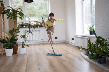 A girl dances with a mop to clean the floor in a new house - general cleaning in an empty room, the...
