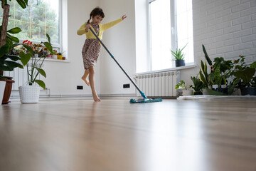 A girl dances with a mop to clean the floor in a new house - general cleaning in an empty room, the...