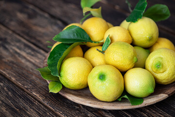 Fresh ripe lemons with green leaves on wooden table
