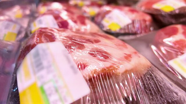 Raw pork fillets or steaks in cling-wrap plastic containers are in a supermarket refrigerator. Close-up