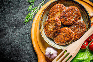 Cutlets at the old pan with a spatula, cherry tomatoes and salad leaves.