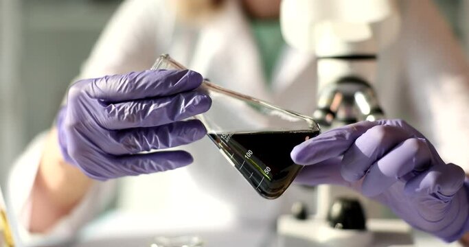 Laboratory flask with crude oil in hands of chemist