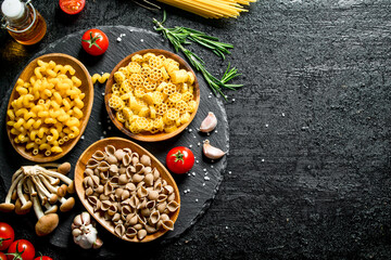 Different kinds of raw paste in bowls with tomatoes, garlic and mushrooms.
