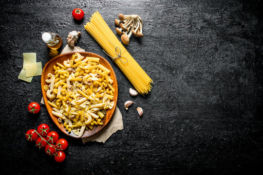 Different kinds of raw pasta with cheese slices, mushrooms and tomatoes.