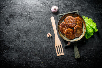 Cutlets in pan with garlic,salad leaves and a wooden shovel.