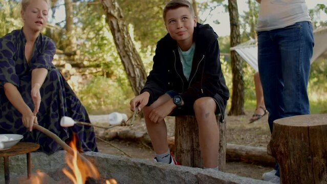 Smiling boy toasting a marshmallow during a family campfire in summer