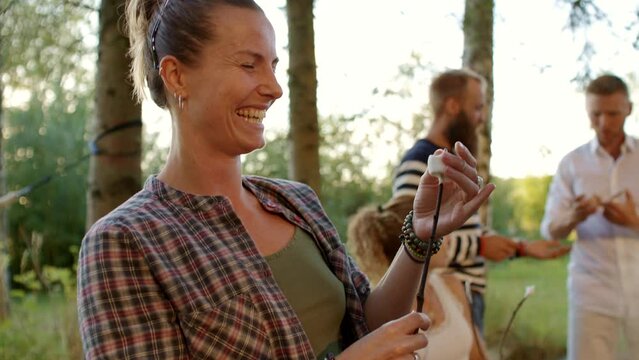 Smiling woman putting a marshmallow on a stick during a family campfire outside in summer