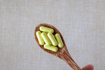 Yellow quercetin capsules in a wooden spoon on a beige background. Dietary supplement, vitamin or...