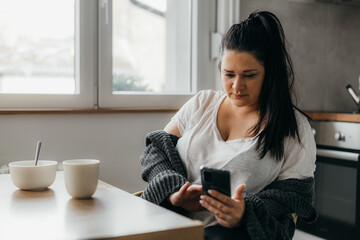 Adult woman checks her phone in the kitchen