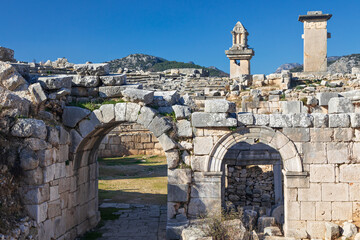 Entrance gate to theatre of Xanthos ancient city - part of Lycian way. Tomb monument of king Kybernis ( Harpy Tomb), Pillar Tomb on background. Popular travel destination in Antalya, Turkey