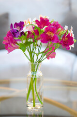 Beautiful bouquet in a vase on a glass table. Blooming pink, purple Alstroemeria. Home decor and decoration. Beautiful petals and green leaves in a floral arrangement.