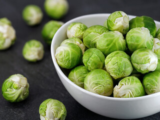 Close up of organic brussel sprouts in a white bowl on black stone background