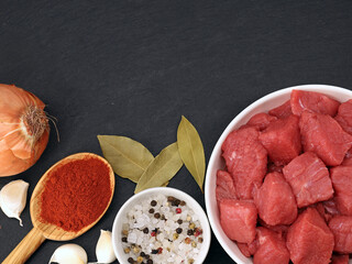 raw diced beef with onions, garlic and spices on a black stone board, top view of the ingredients for a goulash with copy space