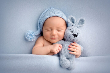 A cute newborn boy in the first days of life sleeps naked on a blue fabric background. The kid...