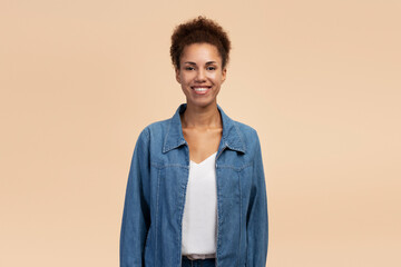 Smiling beautiful African American young woman in casual denim, look at camera over beige background