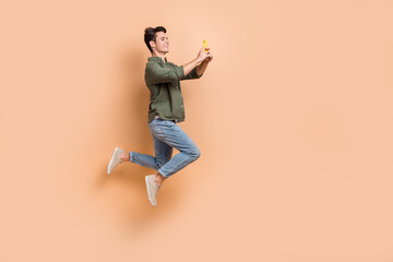 Fototapeta na wymiar Full length photo of young jump carefree guy blogger student selfie cadre new camera smartphone wear khaki shirt isolated on beige color background