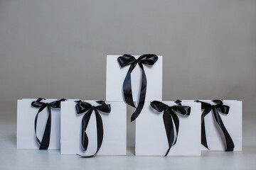 Five white paper gift bags with black bows on a gray background