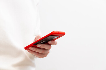 Close up of female hand holding credit card and using smartphone in red case on white background. Woman paying securely online, using banking service, ordering in internet store. Online shopping.