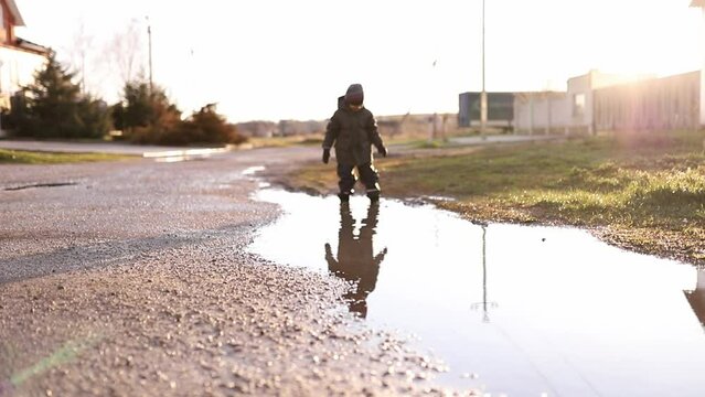 a boy in yellow rubber boots walks through a puddle