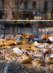 Sweets seen through the shop window. Shop window of a patisserie or bakery with croissants, apple pies, waffles and churros. Freshly baked pastries.