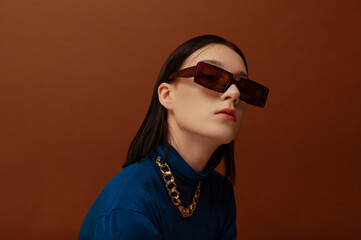 Fashionable confident woman wearing trendy brown rectangular sunglasses, chunky chain, stylish blue...