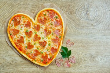 Heart shaped pizza with heart shaped salami on parchment paper with wooden background.Creative art...