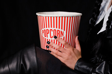 Vinnytsia, Ukraine. January 16, 2023: A brunette with two pigtails in a black dress holds a box of popcorn. Wednesday series from Netflix. Copy space