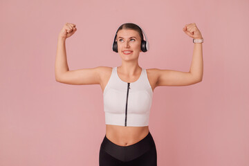 Young cheerful caucasian woman showing biceps and looking up over pink background. Portrait of...