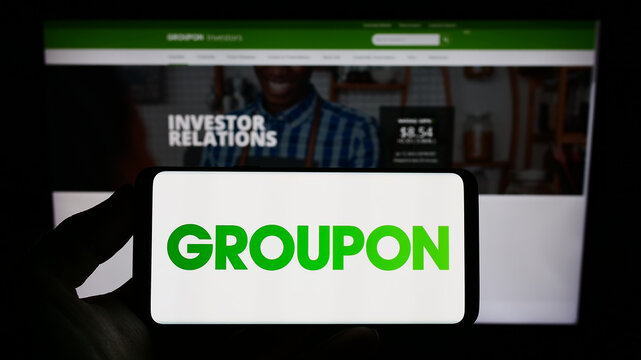 Stuttgart, Germany - 01-13-2023: Person holding smartphone with logo of US e-commerce company Groupon Inc. on screen in front of website. Focus on phone display.