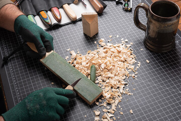 Carving tools, sharping knife on a leather strop. Cutting mat with basswood, shavings, gloves,...