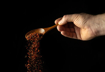 Mixture of dry spices is poured from a wooden spoon in the cook hand. Free space for advertising on...
