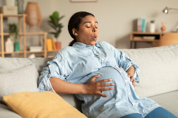 African american pregnant woman touching belly, suffering painful contractions and making breathing...