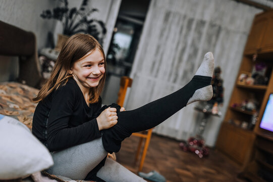 Little Diligent Girl, The Child Puts Black Pants On Her Feet In The Room, Sitting On The Bed.