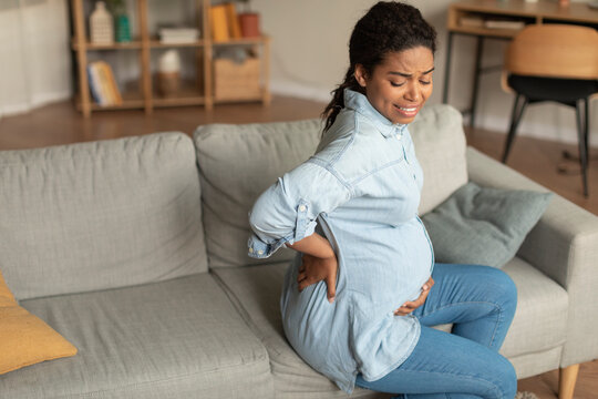 Sad Black Pregnant Lady With Big Belly Suffering From Back Pain, Sitting On Sofa In Living Room, Free Space