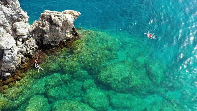 Aerial view of a young couple snorkeling above coral reef reaching deeper parts of the crystal clear water, Rhodes, Greece. Aerial drone view of a couple snorkeling swimming in crystal clear water.