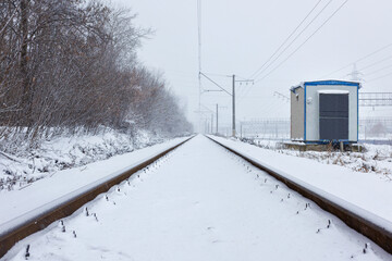Snowfall covers the railroad yard and the transformer box with fluffy snow.