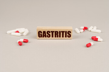 On a gray surface are tablets, capsules and a wooden plate with the inscription - Gastritis