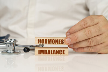 On a white surface, a stethoscope and wooden plates with the inscription - Hormones Imbalance