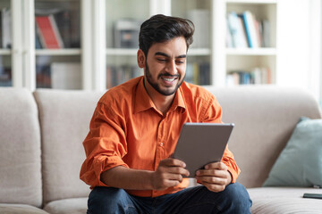 Happy middle eastern guy using digital tablet at home