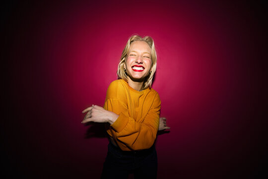 A happy young blond woman is laughing while standing in front of the magenta background. Viva magenta.