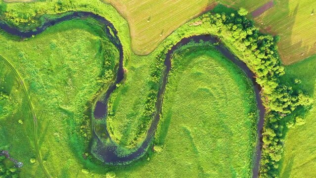 Top smooth rotation decrease aerial view of the natural landscape valley of a meandering river among green fields and forests