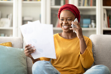 Black lady holding papers and talking on phone at home