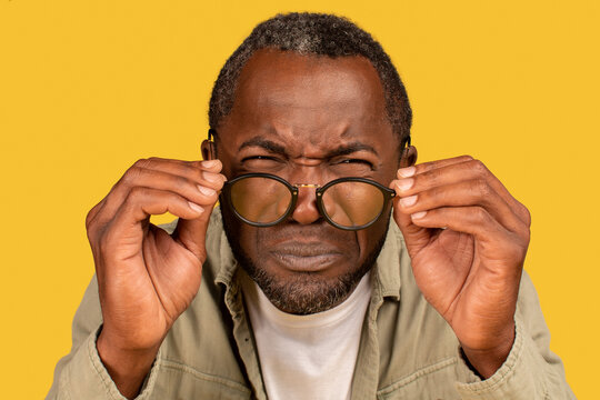 Concentrated african american middle aged man squinting eyes, takes off glasses, looks at camera