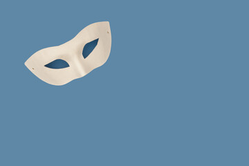 White domino mask against blue background with copy space. Carnival mood. Minimalist flat lay.