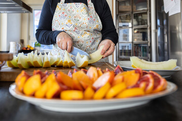 A woman in a kitchen apron prepares a bright slice of fruit