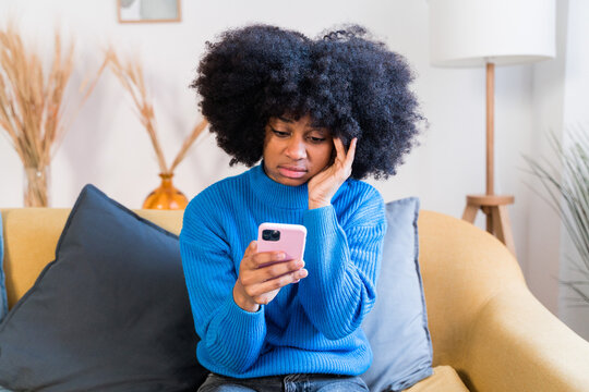 Concerned Black Woman Using Smartphone On Sofa