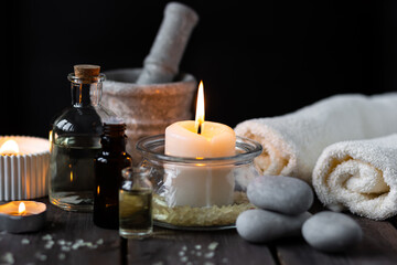 Fototapeta na wymiar Spa setting with essential oil, candle, sea salt, pebbles, towel on dark wooden background. Massage, aromatherapy. Natural organic ingredients for relaxation, detention. Wellness in salon concept
