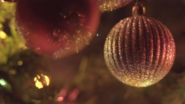 Christmas ornaments hanging on tree, shining while lights flash in background