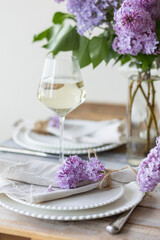 Beautiful table decor for a wedding dinner with a spring blooming lilac flowers. Celebration of a special event. Fancy white plates, wineglasses. Countryside style