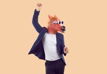 Portrait of strange man wearing T shirt, suit jacket, funny horse mask and sunglasses having fun and dancing isolated on beige background. Fun, party, humor concept - obrazy, fototapety, plakaty